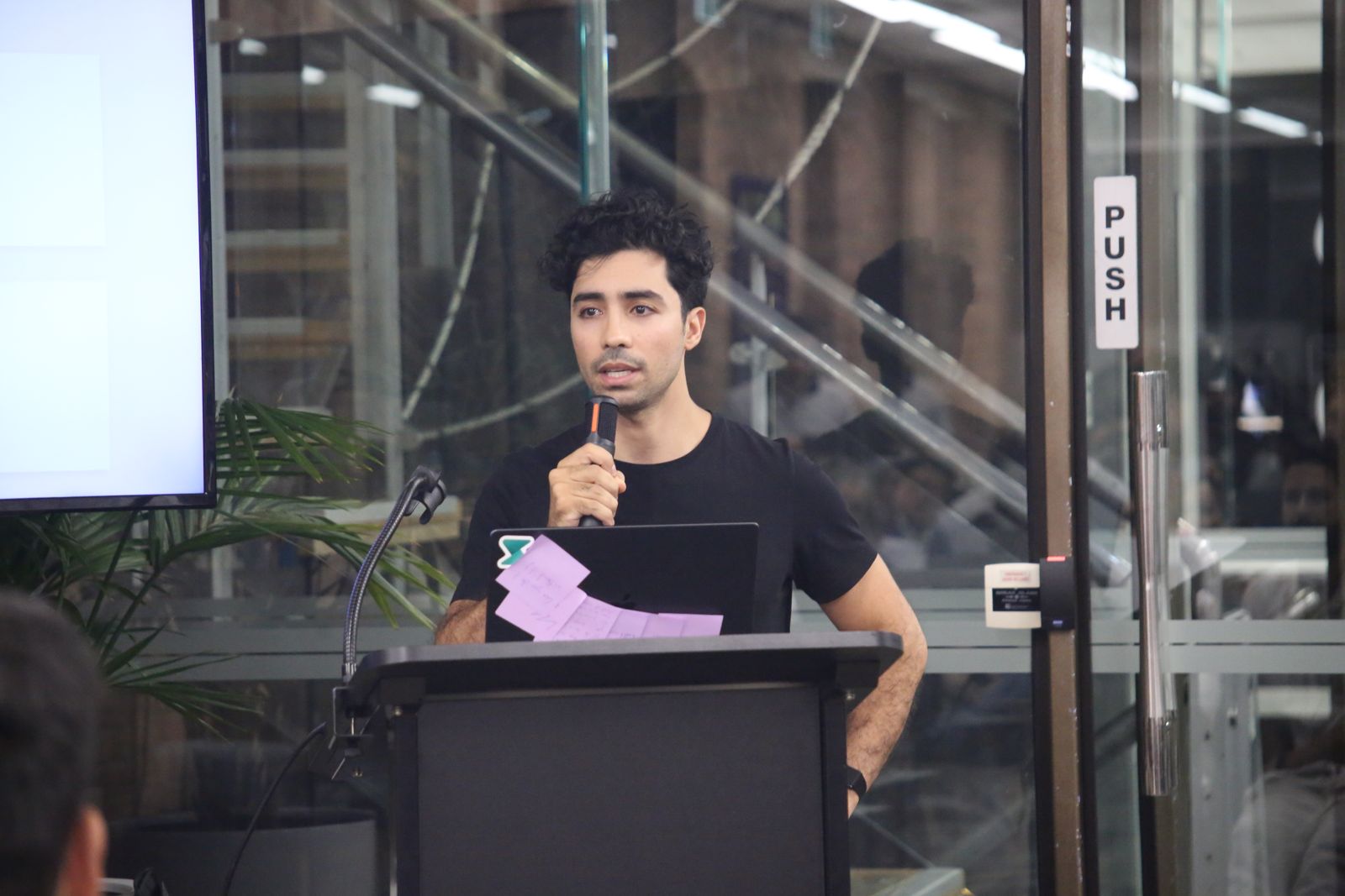 Faisal Taibi speaking into a microphone at a lectern.